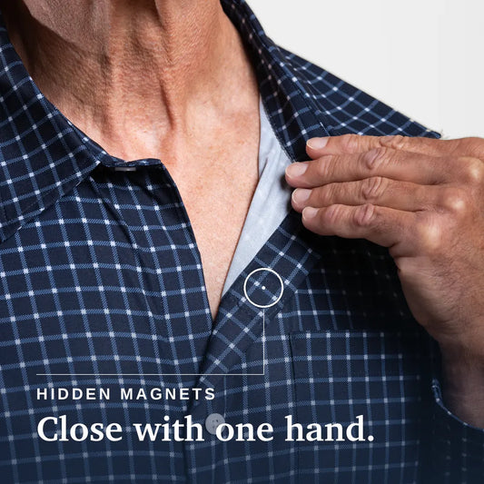A smiling older man standing against a clean white studio background, wearing a blue and white checkered button-down shirt, tan chinos, and white sneakers. #Navy Check