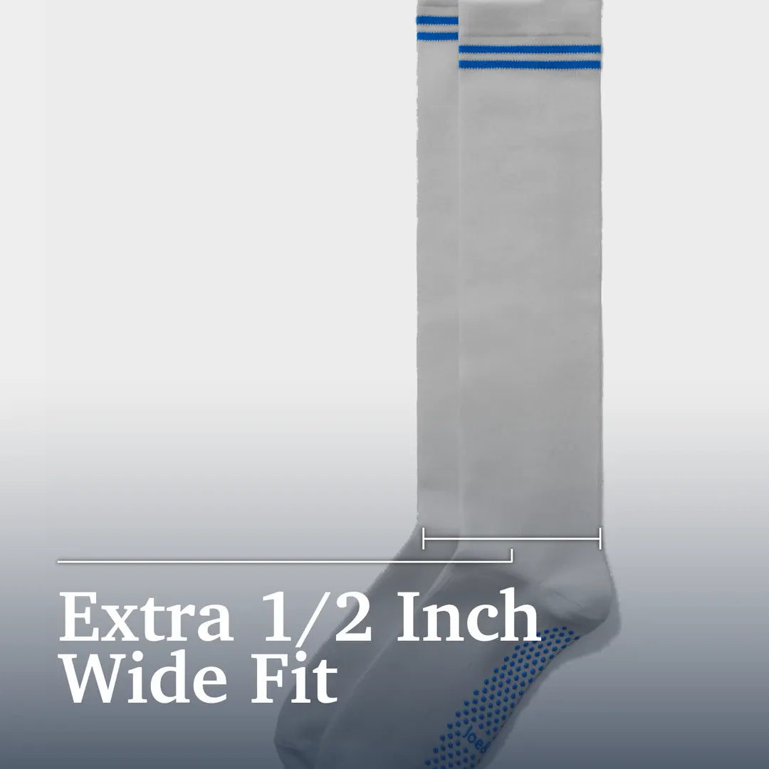 A pair of white wide-fit athletic socks with blue stripes near the top and a blue dotted grip pattern on the sole, shown with text reading 'Extra 1/2 Inch Wide Fit' on a light gray gradient background. Joe & Bella Big-Grip No-Slip Compression Socks: 3-Pack #Grey