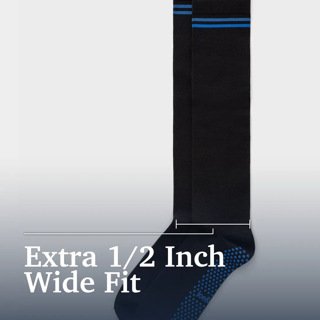 A single black wide-fit sock shown against a light gray gradient background with white text reading 'Extra 1/2 Inch Wide Fit' and a measurement bracket indicating the width. The sock has blue horizontal stripes near the top and a blue dotted grip pattern on the sole. Joe & Bella Big-Grip No-Slip Compression Socks: 3-Pack #Black