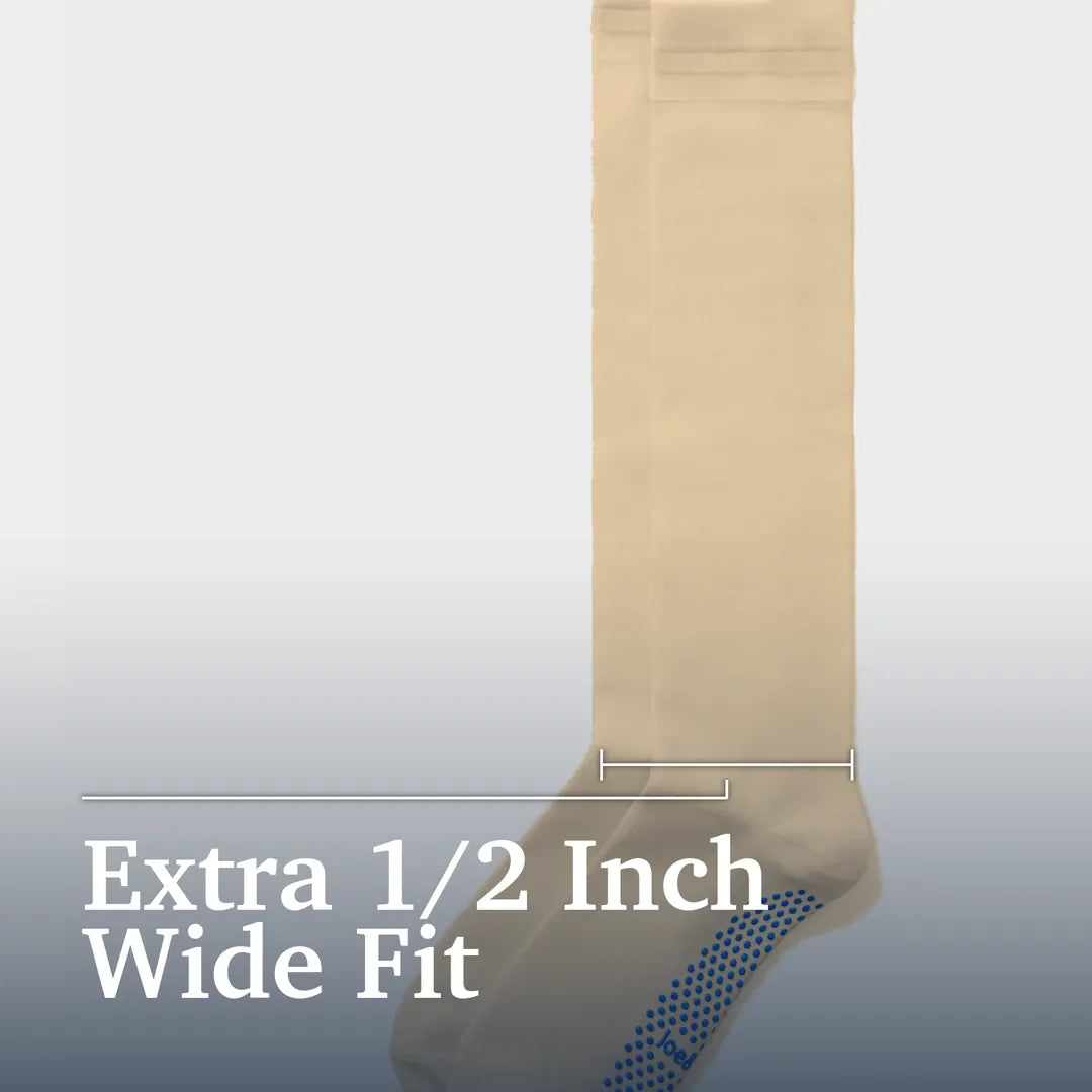 ["A single beige wide-fit sock shown against a light gray gradient background with text reading 'Extra 1/2 Inch Wide Fit' and a measurement bracket indicating the width. Joe & Bella Big-Grip No-Slip Compression Socks: 3-Pack ", "Beige"]
