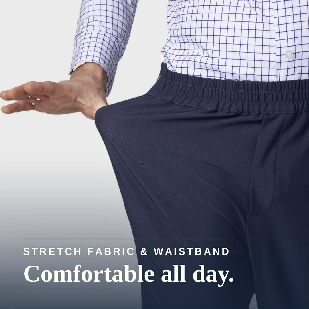 A close-up of a person wearing dark navy elastic-waist pants and a white button-up shirt with a blue grid pattern, stretching the fabric of the pants to demonstrate elasticity. White text at the bottom reads 'STRETCH FABRIC & WAISTBAND' and 'Comfortable all day. Joe & Bella CareZips® Men's Access Pants #Dark Navy