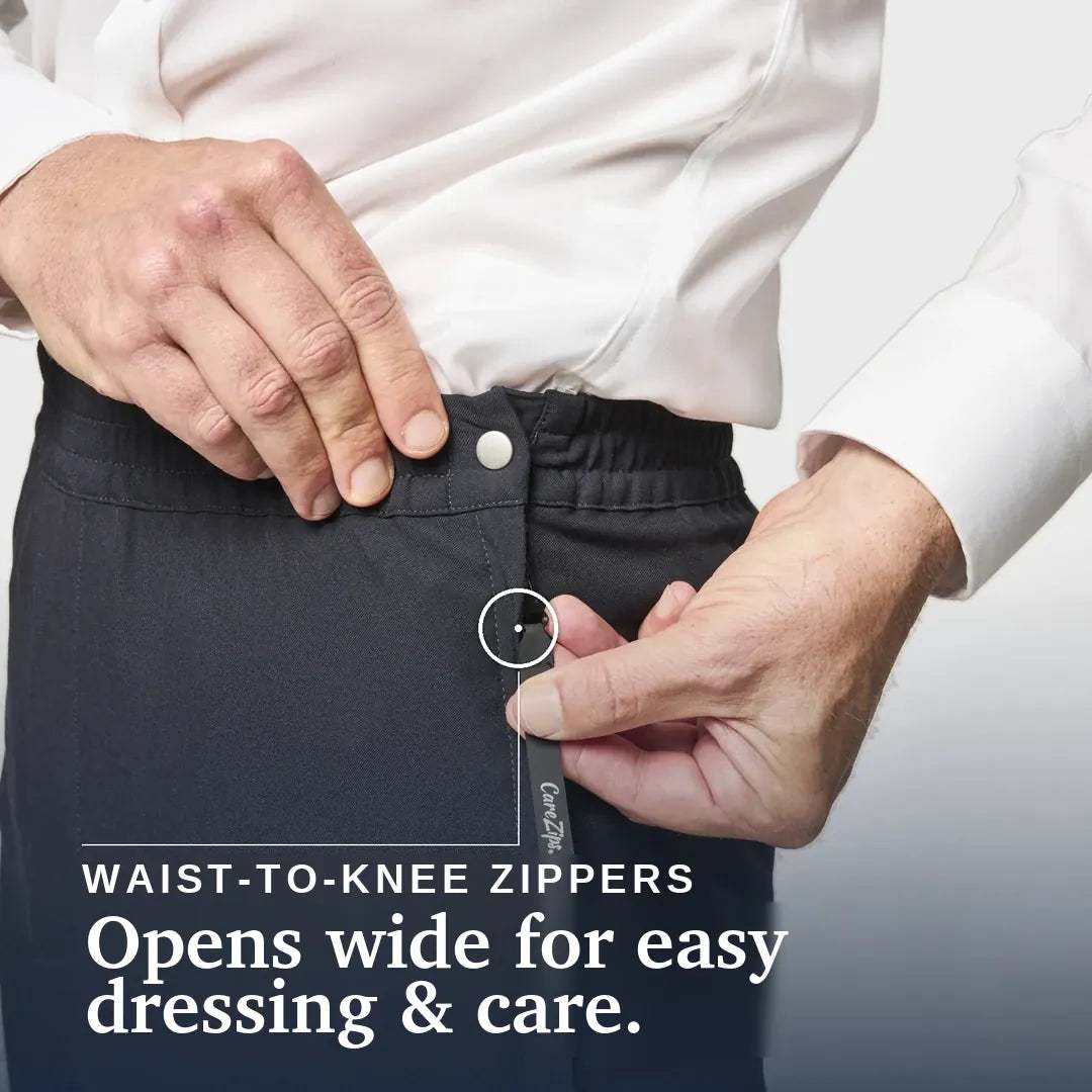 Close-up of a person wearing dark charcoal knee-high compression or medical pants, demonstrating a waist-to-knee zipper that opens wide. The person is wearing a white dress shirt. Joe & Bella CareZips® Men's Adaptive Pants #Black