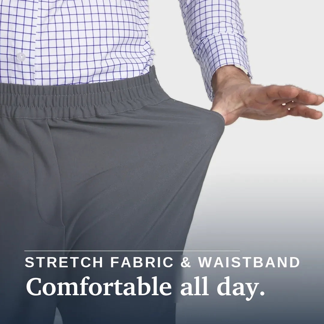 A close-up of a person wearing gray elastic-waist pants, pulling the fabric outward with one hand to demonstrate stretch. The person is also wearing a blue and white checkered shirt. Joe & Bella CareZips® Men's Access Pants #Slate Grey
