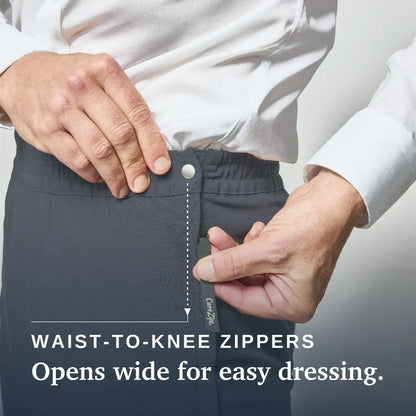 Close-up of a person wearing dark gray zippered pants, demonstrating a waist-to-knee zipper with a white shirt. Text on the image reads 'WAIST-TO-KNEE ZIPPERS' and 'Opens wide for easy dressing & care. Joe & Bella CareZips® Men's Access Pants #Slate Grey