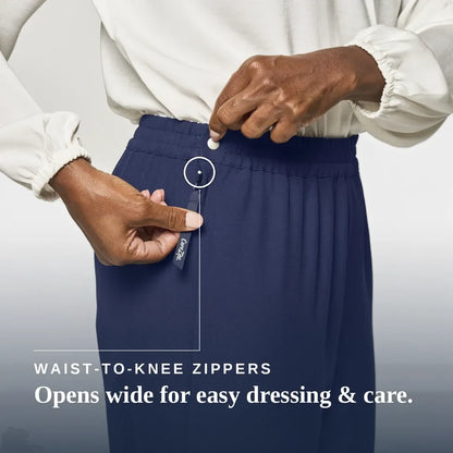 A close-up of a person wearing navy blue waist-to-knee zippers pants, demonstrating how easily the waistband can be opened. The person is wearing a white long-sleeve blouse, and the image includes the text 'WAIST-TO-KNEE ZIPPERS Opens wide for easy dressing & care. Joe & Bella CareZips® Women's Access Pants #Navy