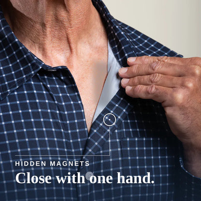 Close-up of a man's neck and chest wearing a navy and white plaid button-up shirt, with his hand reaching toward a small hidden magnet near the collar. Text on the image reads 'HIDDEN MAGNETS Close with one hand. Tailored-Fit #Navy Check