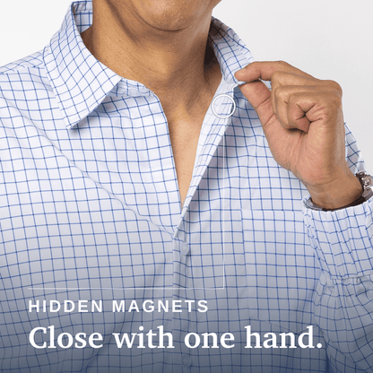 Close-up of a person wearing a white button-up shirt with a blue grid pattern, opening the collar with one hand. White text at the bottom reads 'HIDDEN MAGNETS Close with one hand. Joe & Bella Everyday Magnetic Button-Down for Men | Tailored-Fit #White Check