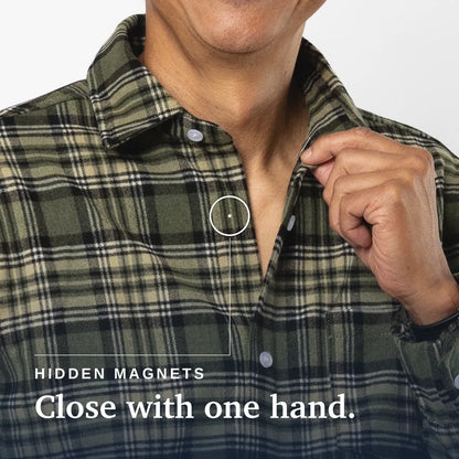Close-up of a man wearing an olive green plaid button-up shirt, with his hand pulling the collar open near a small circular inset showing a hidden magnet. Text at the bottom reads 'HIDDEN MAGNETS Close with one hand. Joe & Bella Green Plaid / S Everyday Magnetic Flannel for Men #Green Plaid