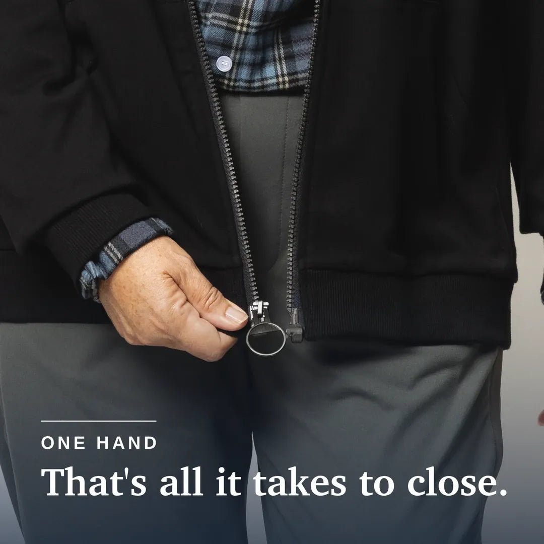 ["Close-up of a person wearing a black zip-front jacket and gray pants, demonstrating one-handed zipper closure with a visible text overlay that reads 'ONE HAND That's all it takes to close.'. Joe & Bella HoodEase™: The Magnetic-Zip-Up Hoodie  ", "Black"]