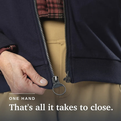 Close-up of a person's hand closing a dark navy zippered jacket, with tan pants and a red plaid shirt visible underneath. White text at the bottom reads 'ONE HAND That's all it takes to close. Navy blue hoodie with a zipper on a beige background #Navy