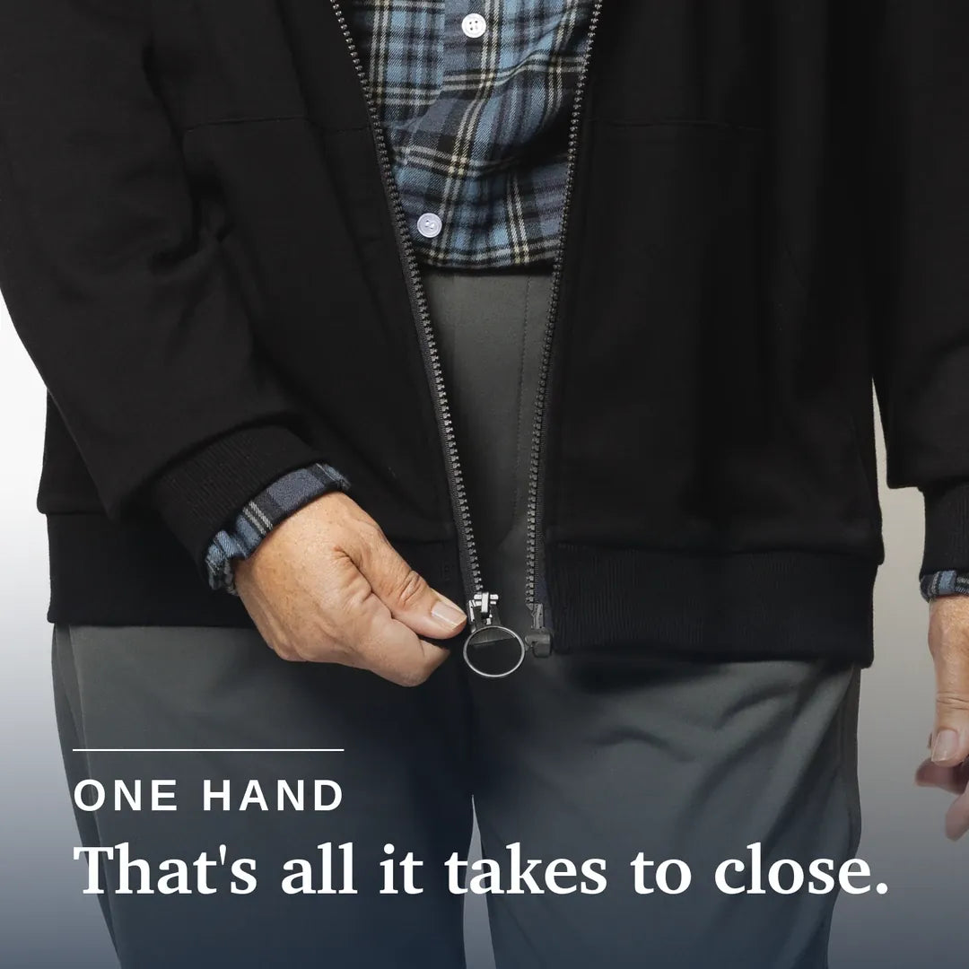 ["Close-up of a person wearing a black zip-front jacket and gray pants, demonstrating one-handed zipper closure with a visible text overlay that reads 'ONE HAND That's all it takes to close.'. Joe & Bella HoodEase™: The Magnetic-Zip-Up Hoodie  ", "Black"]