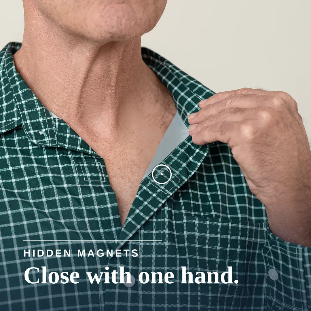 Close-up of a man wearing a green and white plaid button-up shirt, pulling the collar slightly with his right hand. A small inset circle highlights a hidden magnetic area at the collar. Joe & Bella Everyday Magnetic Button-Down for Men | Relaxed-Fit#Green Check