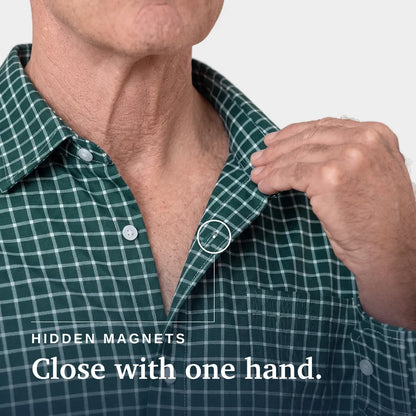 Close-up of a man wearing a green and white plaid button-up shirt, pulling the collar slightly with his right hand. A small inset circle highlights a hidden magnetic area at the collar. Joe & Bella Everyday Magnetic Button-Down for Men | Relaxed-Fit#Green Check