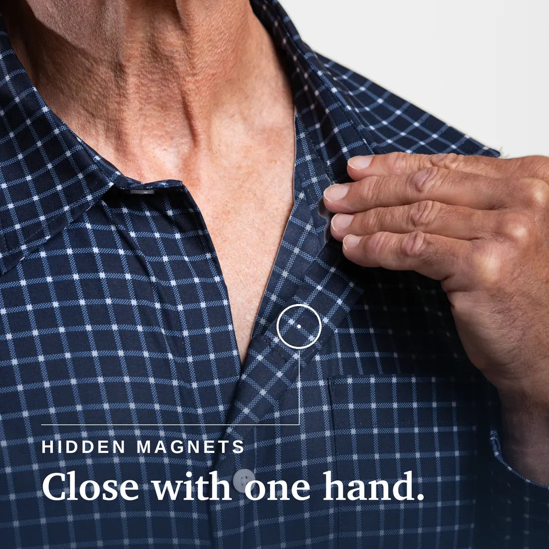 ["Close-up of a man's neck and chest wearing a navy and white plaid button-up shirt, with his hand reaching toward a small hidden magnet near the collar. Text on the image reads 'HIDDEN MAGNETS Close with one hand. Joe & Bella Everyday Magnetic Button-Down for Men | Relaxed-Fit ", "Navy Check"]
