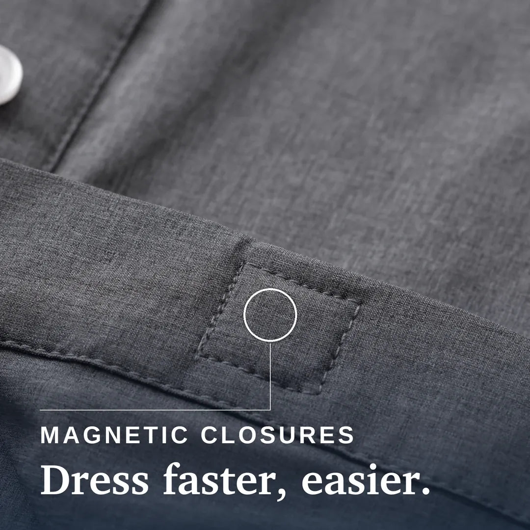 Close-up of a dark gray textured fabric garment showing a stitched pocket or tab with a circular callout and the text 'MAGNETIC CLOSURES Dress faster, easier.'. Joe & Bella Everyday Magnetic Button-Down for Men | Relaxed-Fit #Heathered Grey
