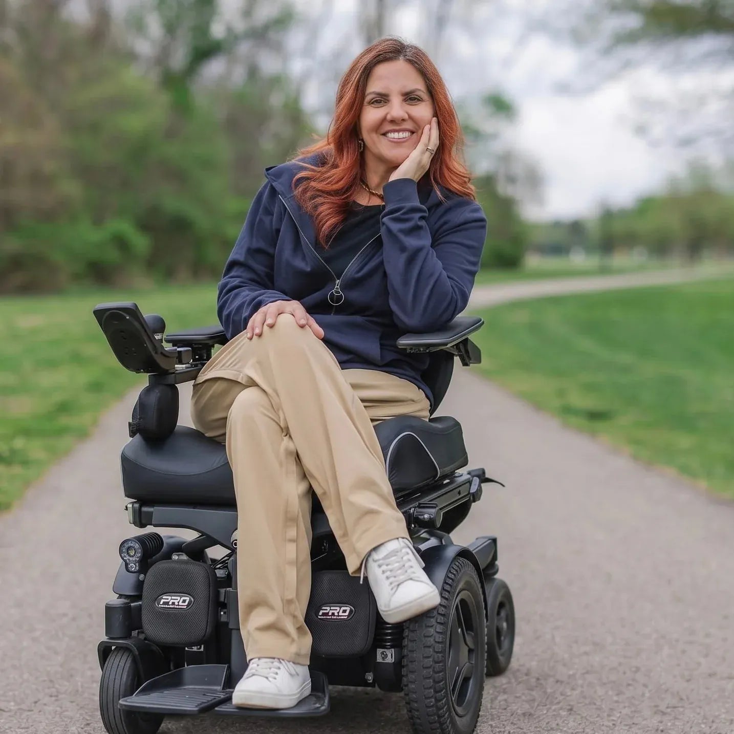 ["Woman in a power wheelchair outdoors on a path with greenery. ", "Navy"]