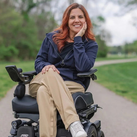 Woman in a power wheelchair outdoors on a path with greenery. #Navy