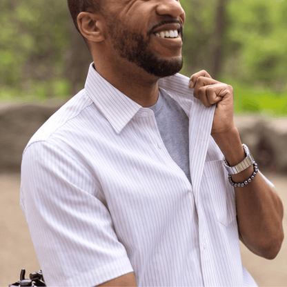 Man adjusting his shirt outdoors with a blurred natural background #Tan Stripe
