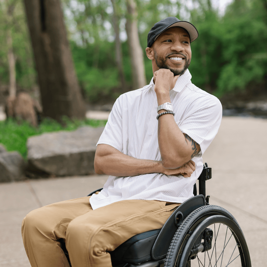 Man in a wheelchair sitting outdoors with trees in the background #Tan Stripe