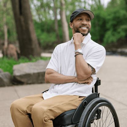 Man in a wheelchair sitting outdoors with trees in the background #Tan Stripe