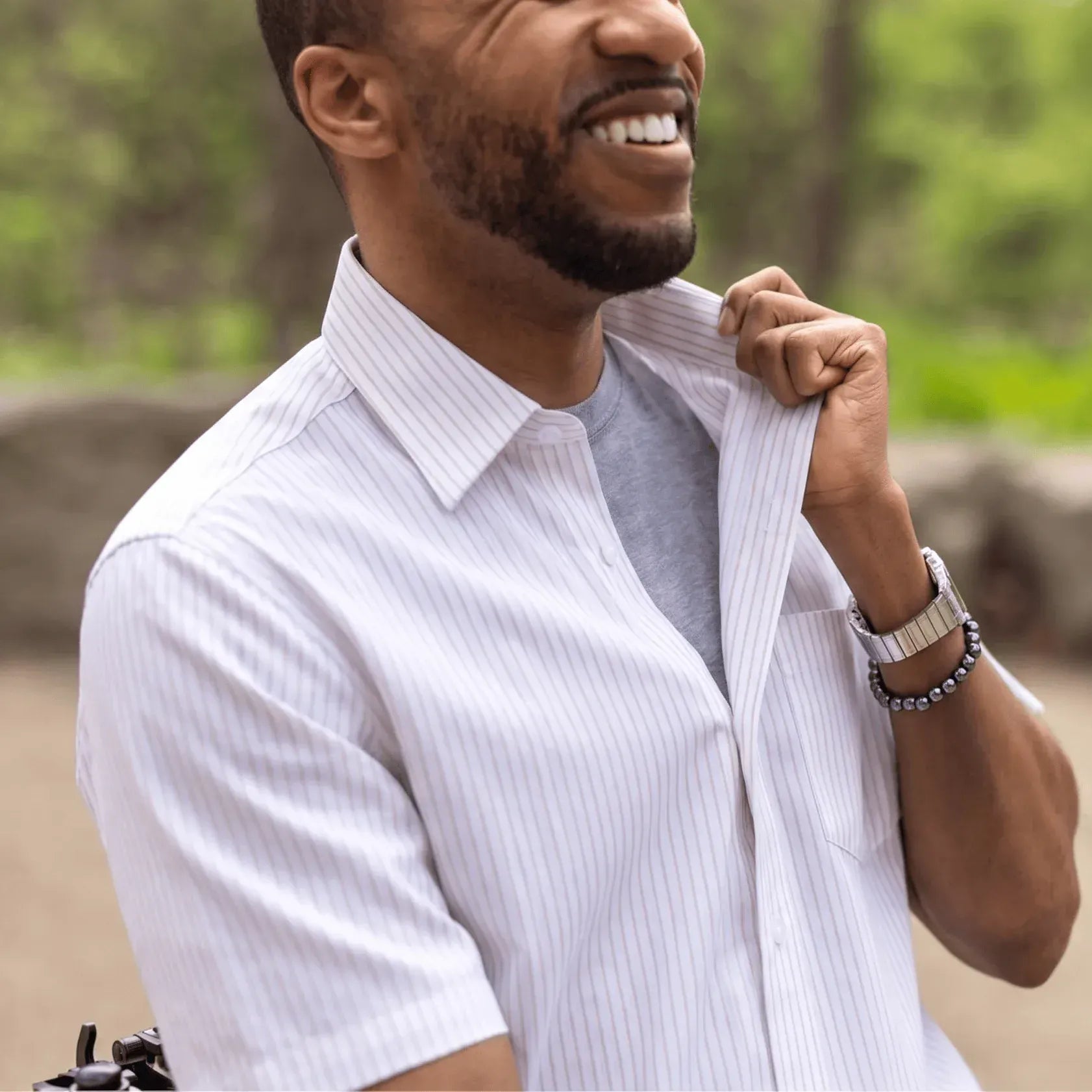 ["Man adjusting his shirt outdoors with a blurred natural background ", "Tan Stripe"]