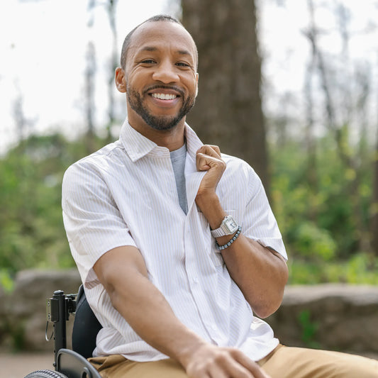 Man in a wheelchair sitting outdoors with trees in the background #Tan 