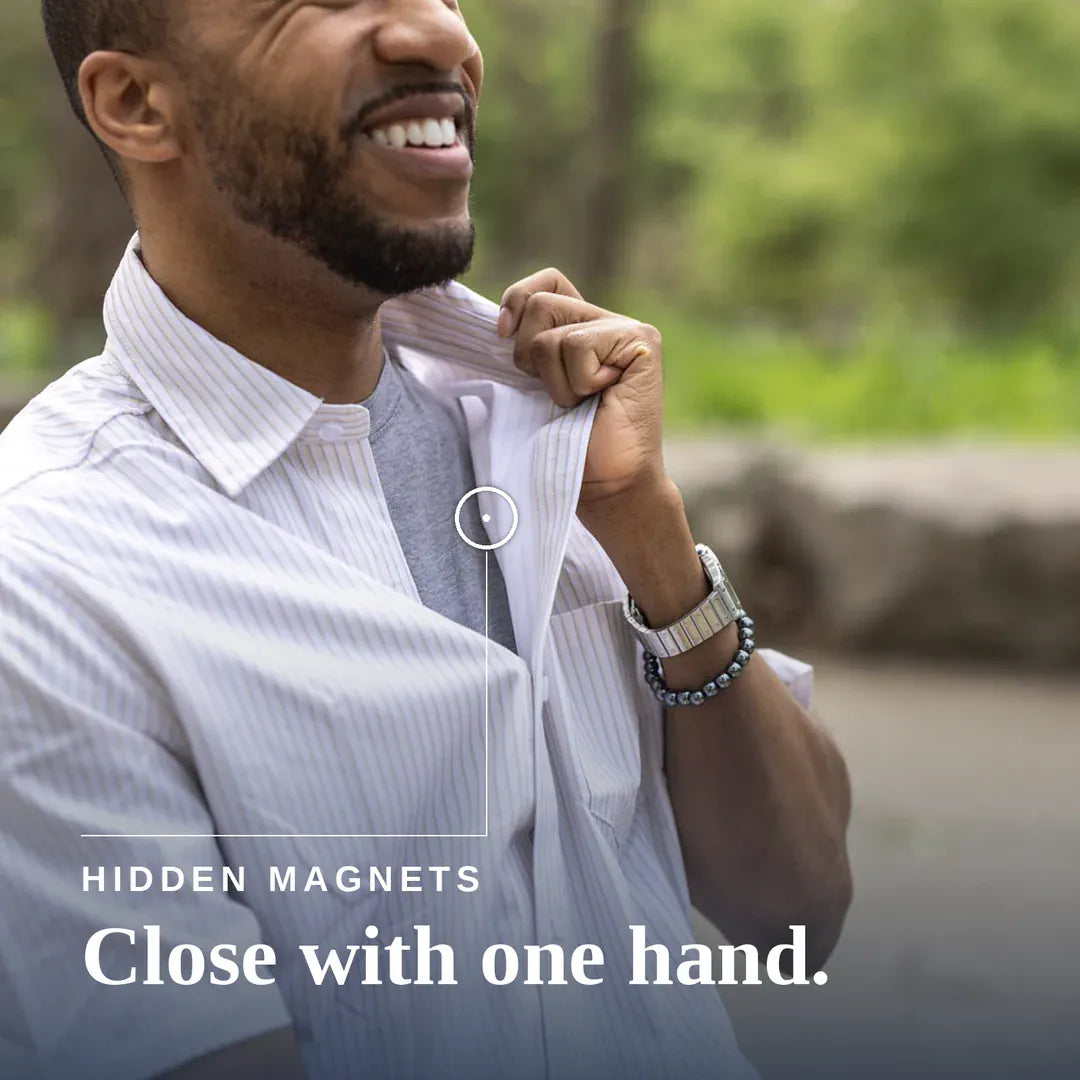 A smiling man in a white pinstripe button-down shirt adjusts the collar with one hand, with a small circular inset showing a hidden magnet feature. Text on the image reads 'HIDDEN MAGNETS Close with one hand. #Tan Stripe