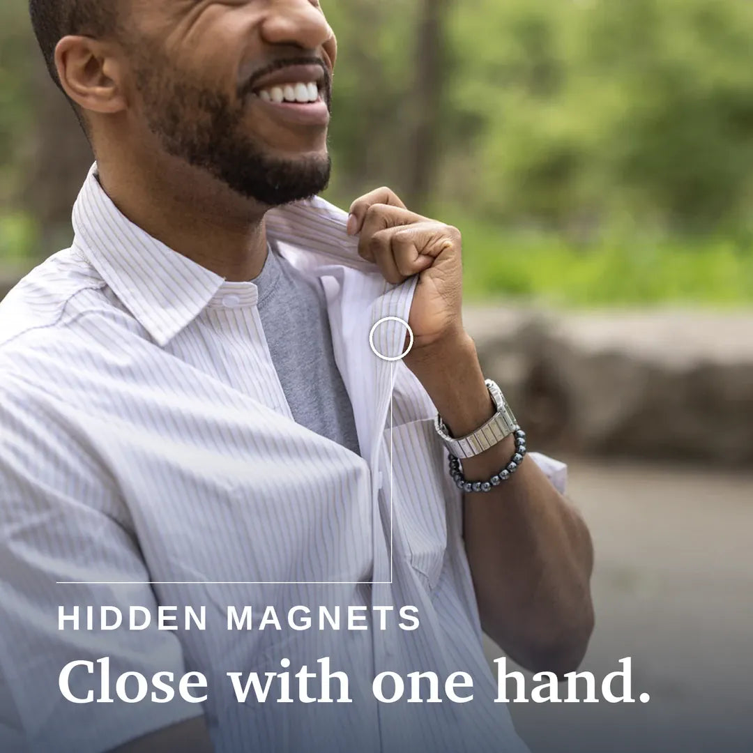 A smiling man in a white pinstripe button-down shirt adjusts the collar with one hand, with a small circular inset showing a hidden magnet feature. Text on the image reads 'HIDDEN MAGNETS Close with one hand. #Tan Stripe