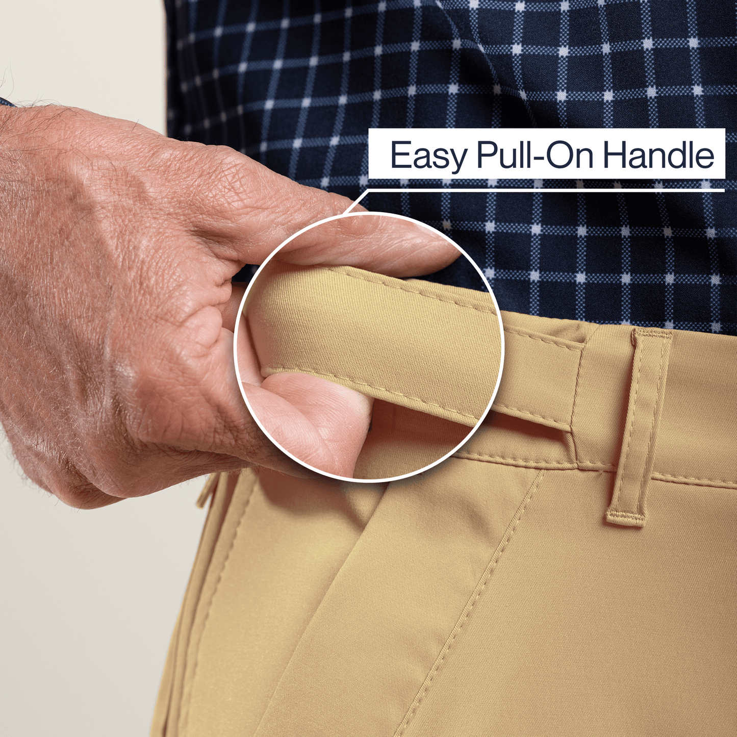 Close-up of a hand using an easy pull-on handle on beige pants with a plaid shirt in the background. #Khaki