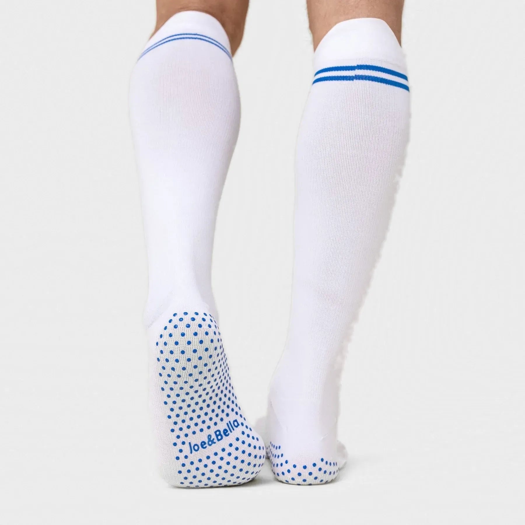 ["White knee-high compression socks with blue stripes at the top and blue grip dots on the sole, shown on a model's legs against a light gray background. Joe & Bella Big-Grip No-Slip Compression Socks: 3-Pack ", "White"]