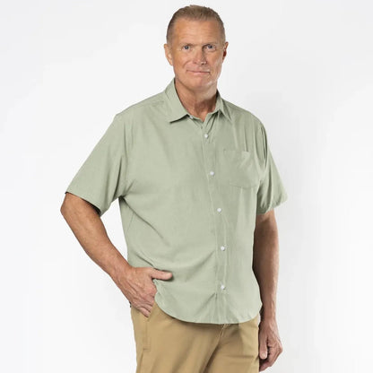 A man modeling a short-sleeve button-up shirt in sage green and khaki pants, standing against a plain white studio background. Green short-sleeve shirt on a beige background #Sage Green